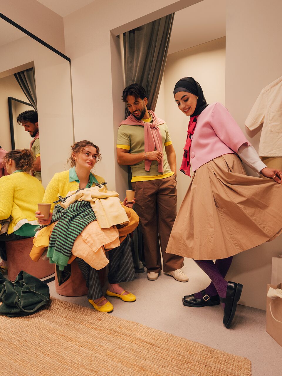 Friends in a fitting room. One girl is over it sitting in a chair buried in piles of clothes